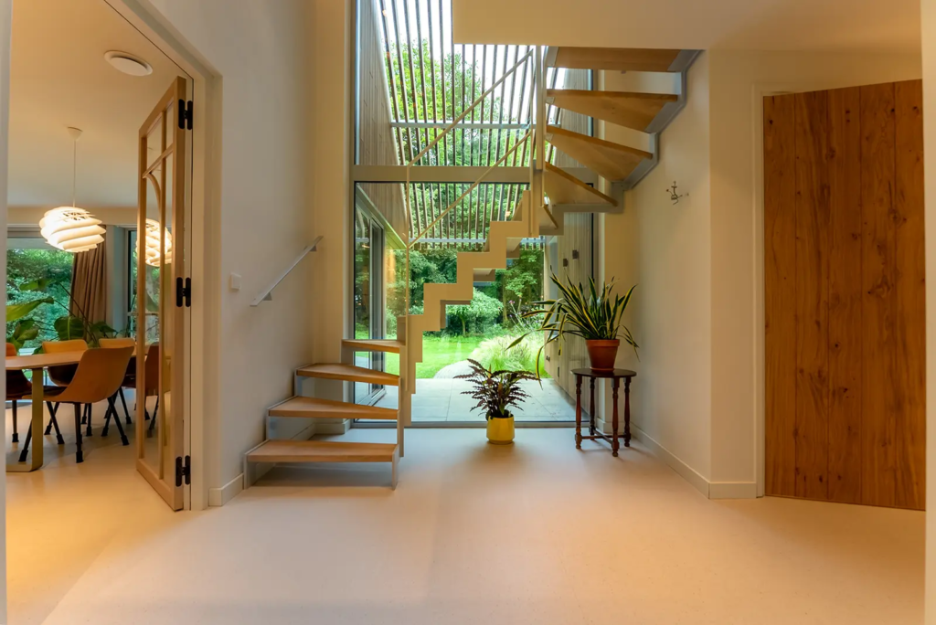 Lichte hal met houten trap en grote raampartijen, verbinding tussen binnen en buiten bij woning in Berkum.