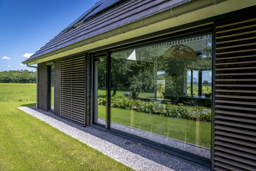 Detail van gevel met grote ramen en houten lamellen ter privacy bij moderne schuurwoning in Olst.