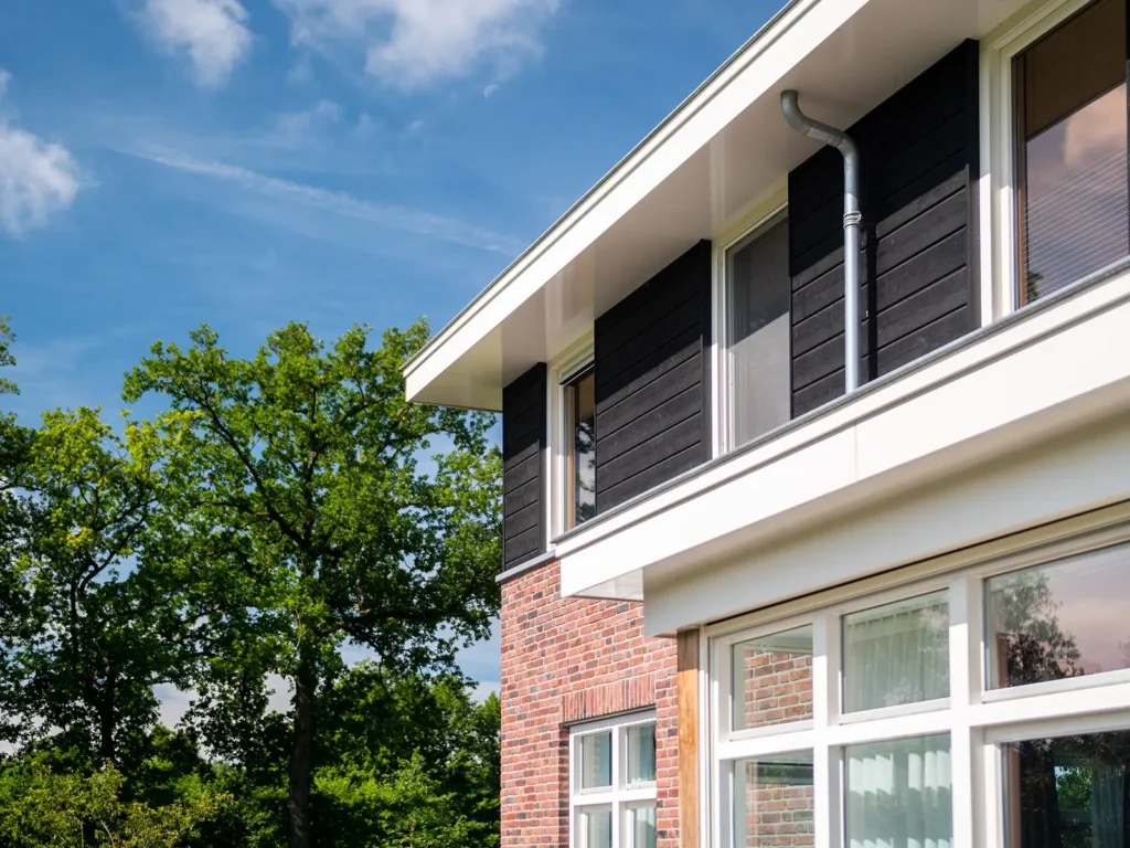 Detail van de gevel van de woning in Heerde met donkere houten luiken, witte kozijnen en metselwerk in warme tinten.