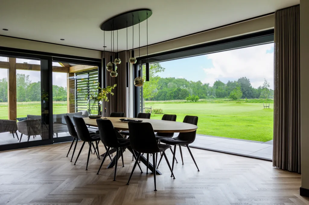 Eetruimte met panoramaraam en volledig openslaande pui in een schuurwoning in Lettele, met zicht op het erf en omliggende groen.