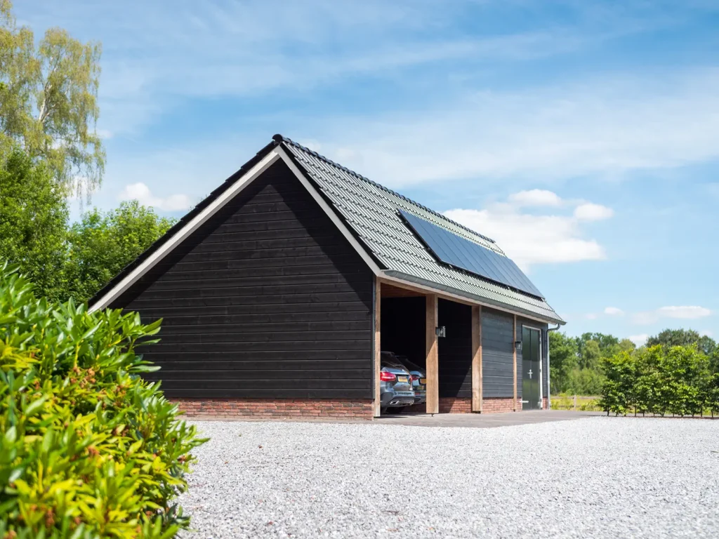Vrijstaande houten schuur bij de woning in Heerde met zwart hout, zadeldak en zonnepanelen.