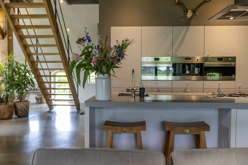 Moderne keuken met trap naar vide, houten balken en landelijke sfeer in woonboerderij Okkenbroek.