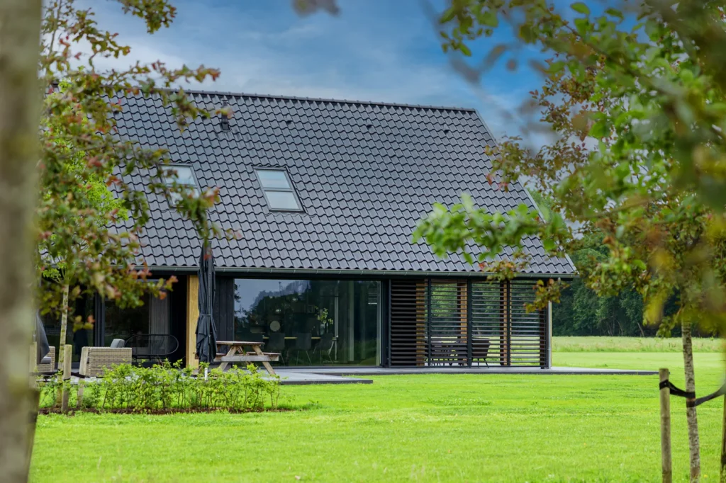 Lange gevelpartij van de schuurwoning in Lettele met houten spanten, grote glasvlakken en donkere verticale gevelbekleding.