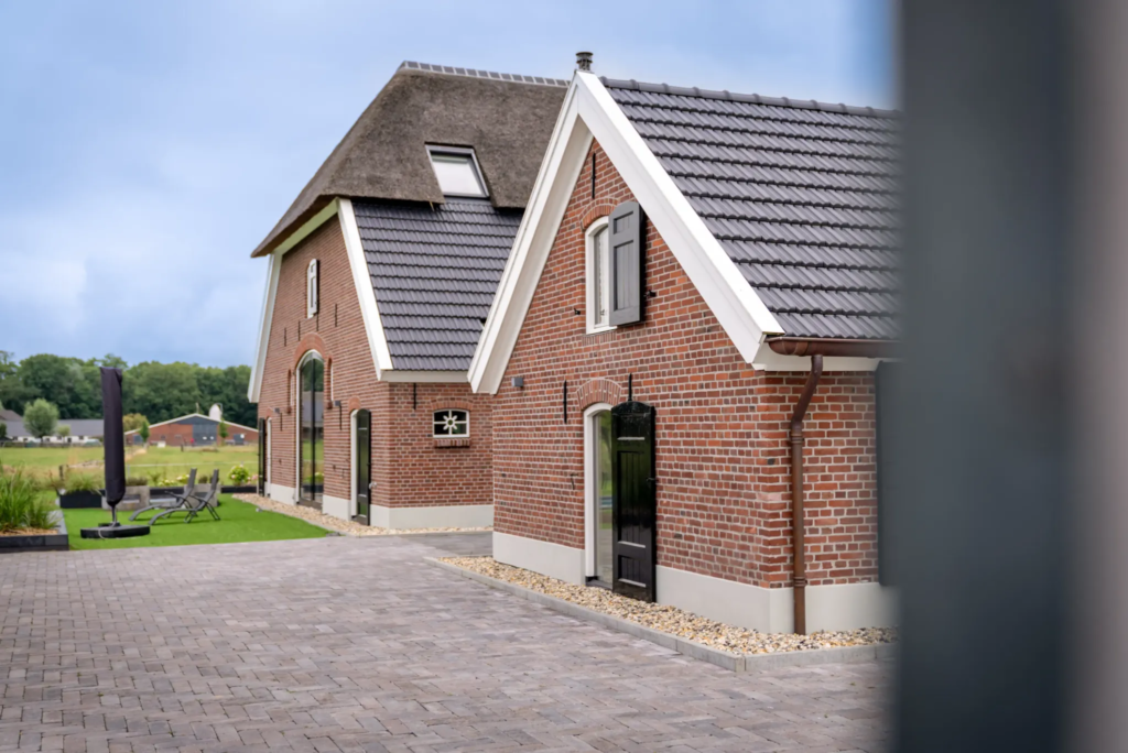 Achterzijde van gerenoveerde woonboerderij en bijgebouw met wolfsdak en rode baksteen in Okkenbroek.