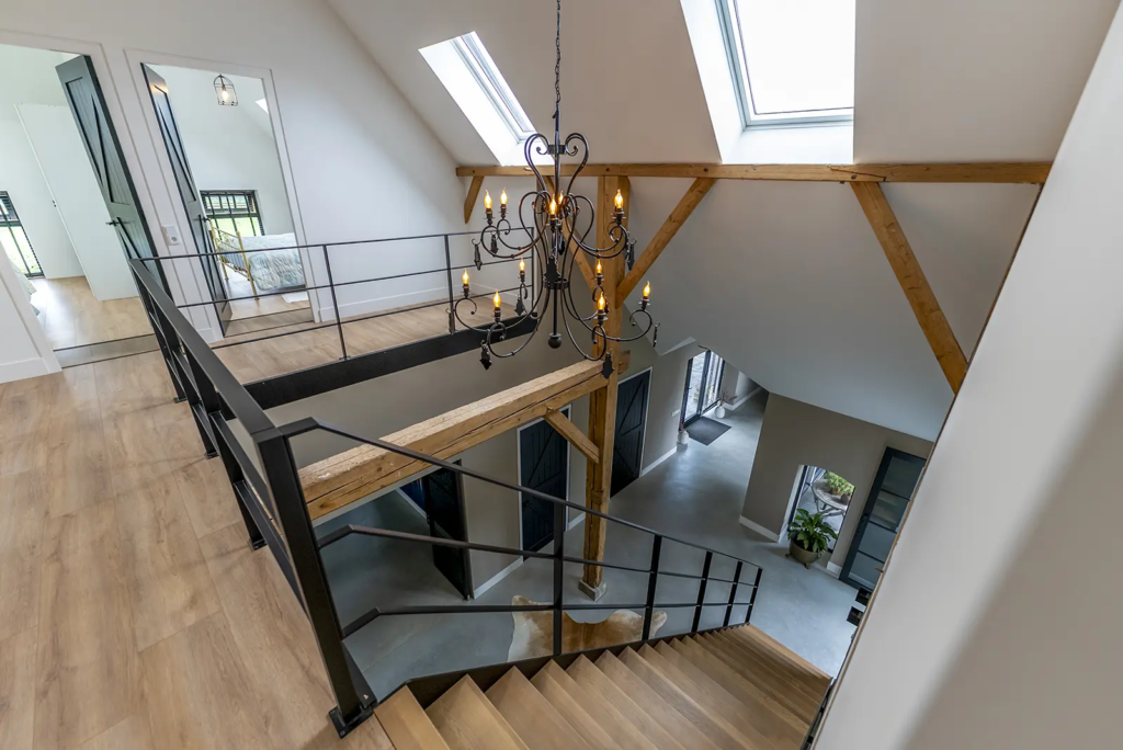 Vide met trap, houten balken en kroonluchter in woonboerderij in Okkenbroek.