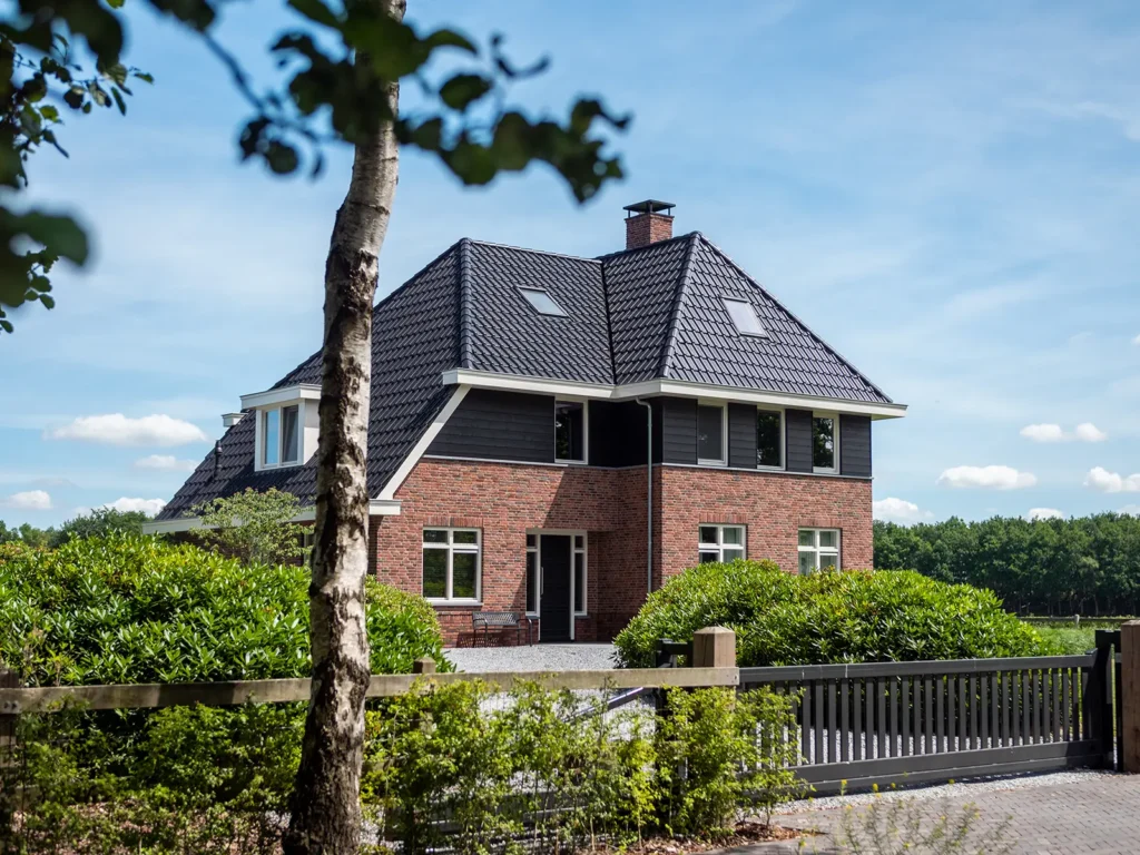 Vooraanzicht van de woning in Heerde met oprit, toegangspoort en klassieke architectuur in een groene omgeving.