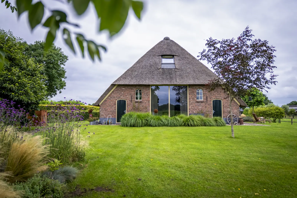 Achterkant van karaktervolle woonboerderij met rieten dak en houten luiken in Okkenbroek.